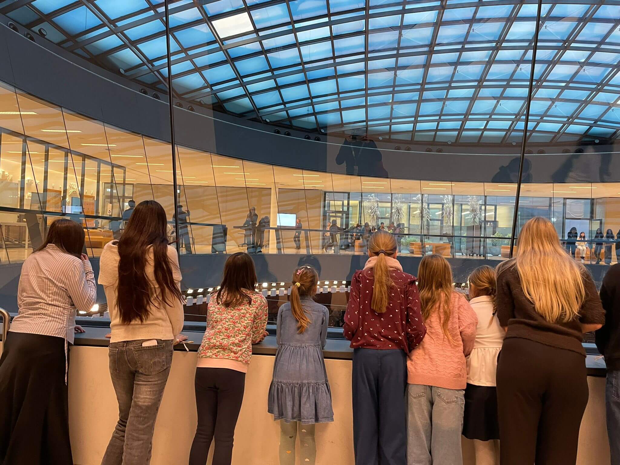 Gruppe Kinder steht vor einer Glaswand und blickt in den Plenarsaal des Nationalrats hinunter.