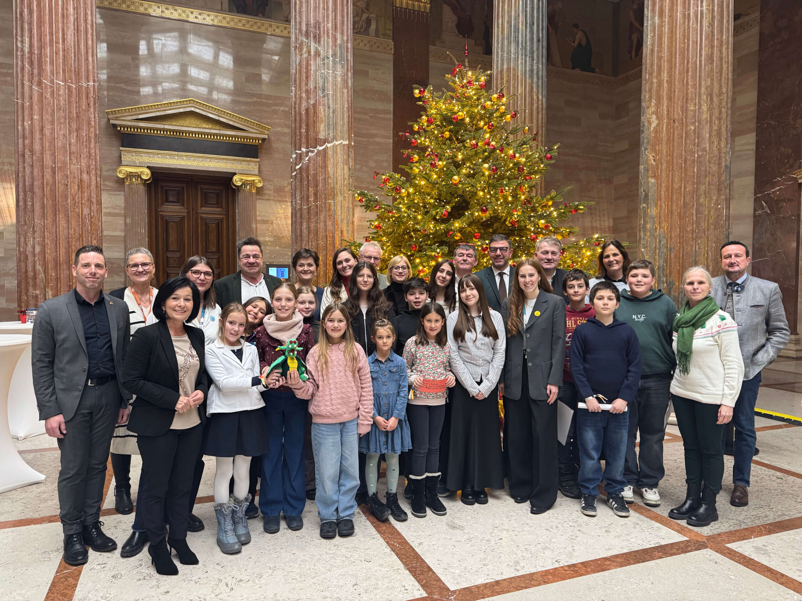 Kinderbeirat_Kinderrechteausschuss (c)BJV_Veraszto (32) Gruppenfoto mit Kindern und Politiker*innen vor einem großen Weihnachtsbaum in der Säulenhalle des Parlaments.